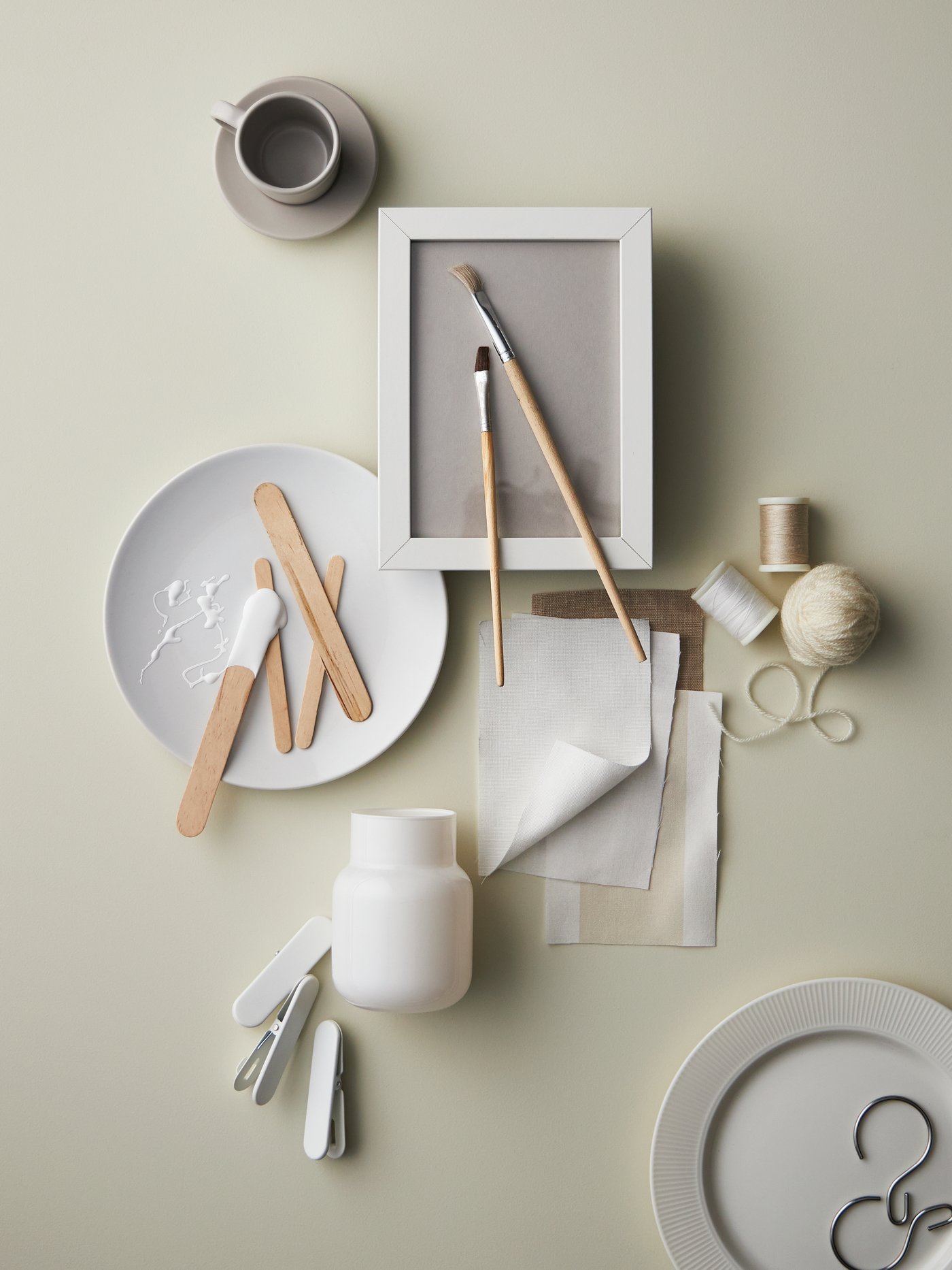Una mezcla dispersa de objetos con un plato auxiliar FLITIGHET blanco, una taza y un platillo de café expreso DINERA beige, tela y cuerda.