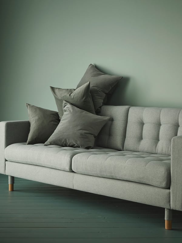 A light green/wood LANDSKRONA 3-seat sofa with four dark green decorative cushions in a living room with green walls.