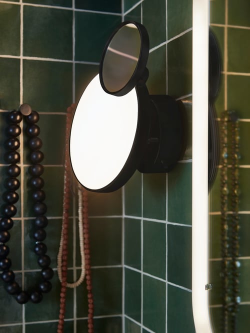 Colț de baie cu o lampă KABOMBA neagră cu perete LED, cu oglindă amplasată lângă o oglindă STORJORM cu iluminare integrată.