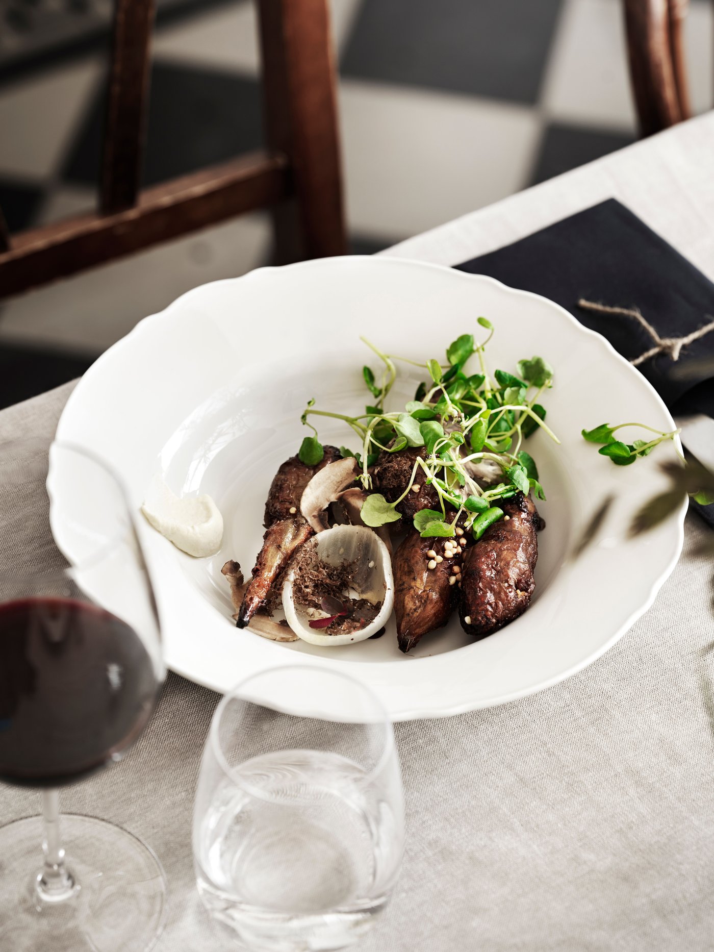 Biały, głęboki talerz UPPLAGA z jedzenim na brązowym stole.