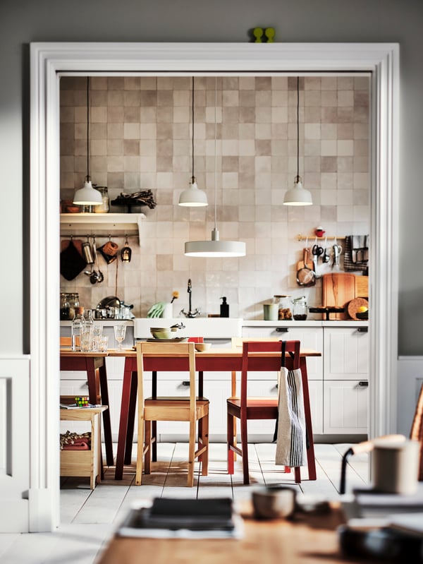 A kitchen with white STENSUND drawer fronts and two PINNTORP tables surrounded by PINNTORP chairs.