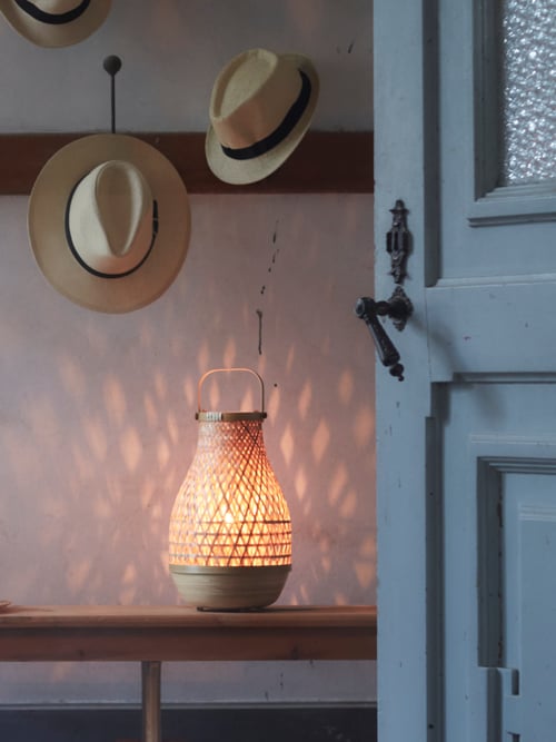 Two hats hanging on a wall above a lamp with a handle, the light from the lamp creating a design effect on the wall.