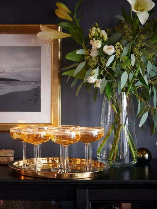 Many STORHET champagne coupes are rimmed with edible gold and are gathered on a brass-coloured tray that sits on a cabinet.
