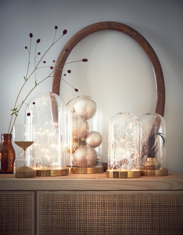 Dispose une petite guirlande lumineuse sur piles dans un globe en verre décoratif et mets-la à côté d’autres globes en verre remplis de décorations.