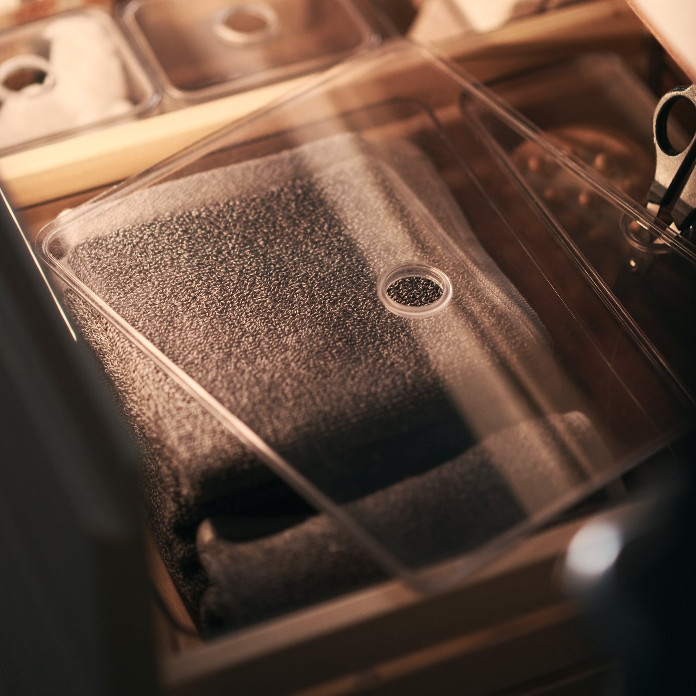 A small bathroom container with a clear lid filled with bathroom accessories including scissors and face flannels.