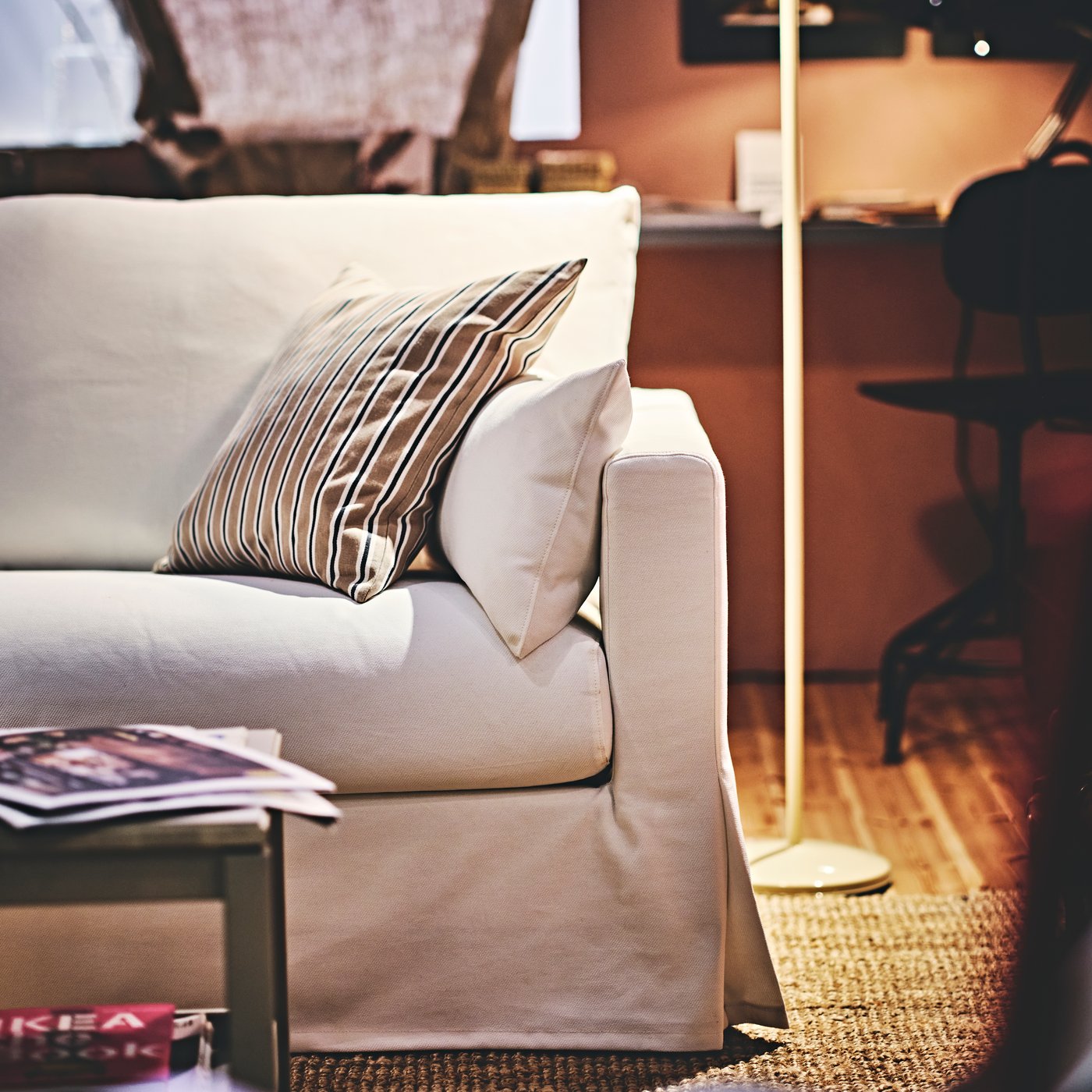 Ein zusätzliches Kissen liegt auf einem weissen HYLTARP 3er-Sofa, das auf einem flach gewebten Teppich steht.