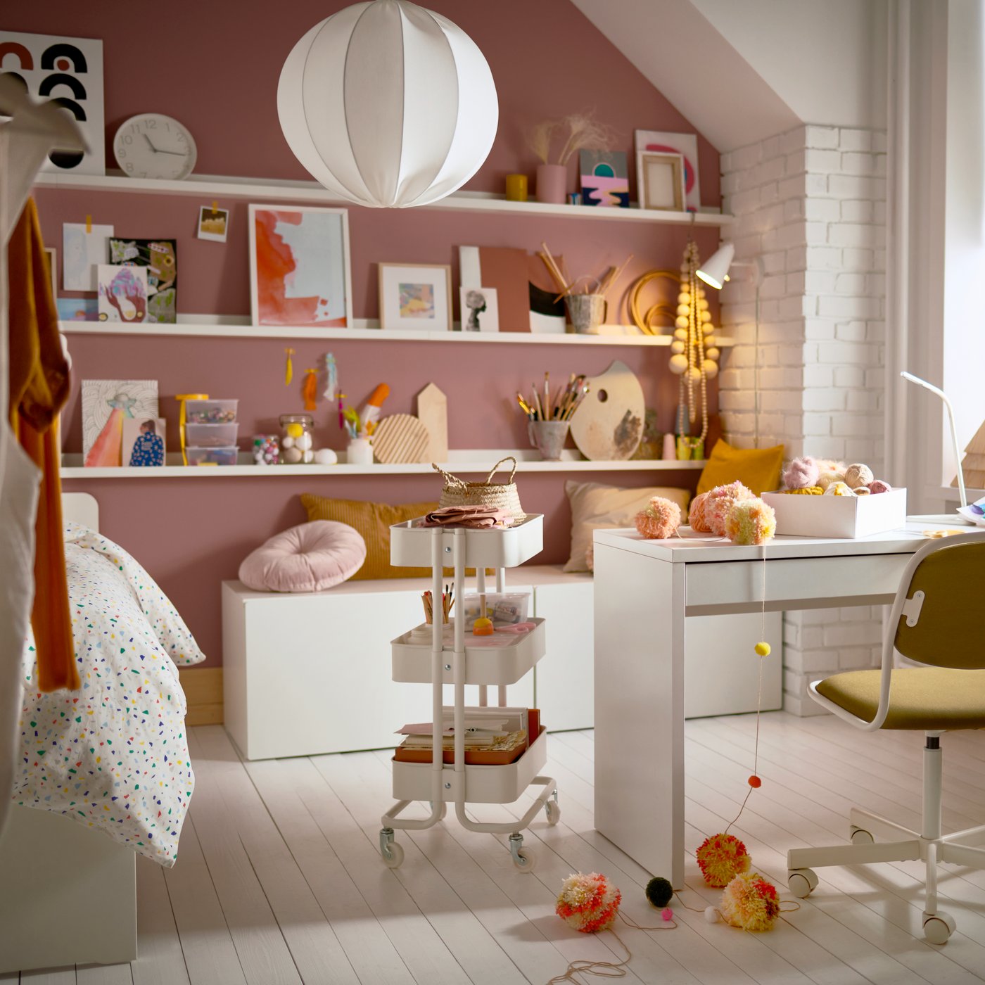 A teenager’s room with a desk, a trolley, picture ledges with artsy decorations, cushions, and a swivel chair.