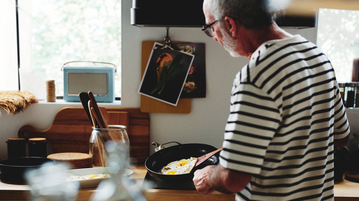 Una persona in una cucina cuoce delle uova in una padella VARDAGEN in acciaio al carbonio accanto a un barattolo VARDAGEN pieno di utensili.