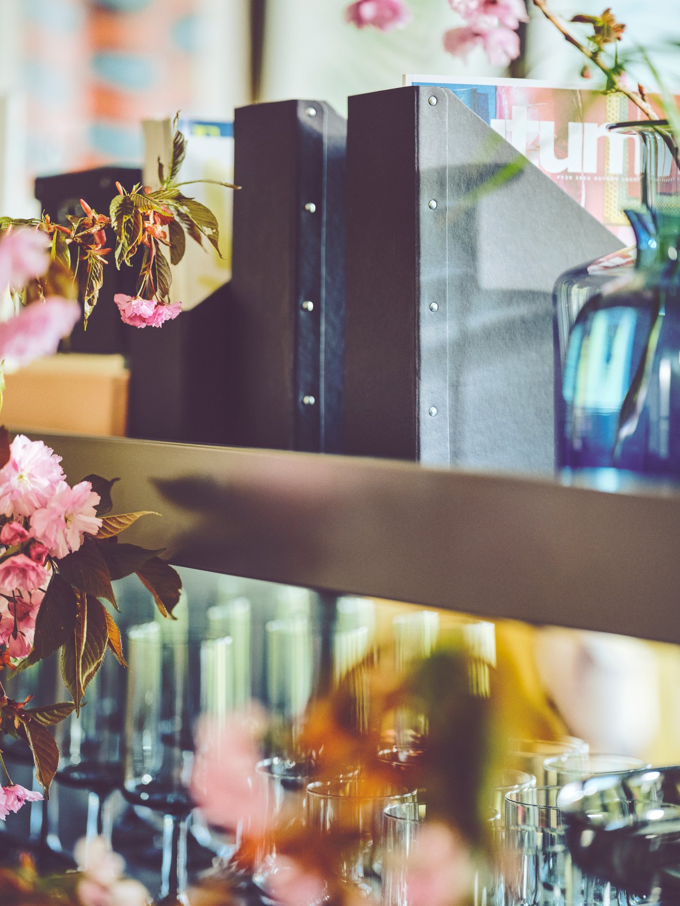 مستويان من الأرفف IDÅSEN بهما ملفا مجلات NIMM، وأوانٍ زجاجية OMBONAD رمادية اللون وزهور مقطوعة في مزهرية.