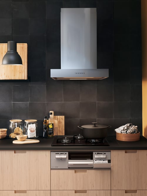 Kitchen with an extractor hood with 3 different speeds, placed above a black casserole with lid, next to a grey pendant lamp.