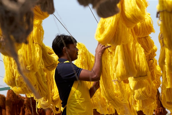 Ein Textilarbeiter in Indien hängt frisch gefärbte Baumwollballen in hellem Gelb zum Trocknen auf.