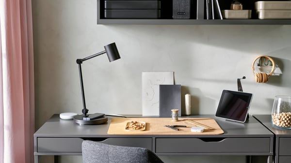 Various smart home office products like a DIRIGERA smart hub, a remote and a lamp with built-in charging are on a grey desk.