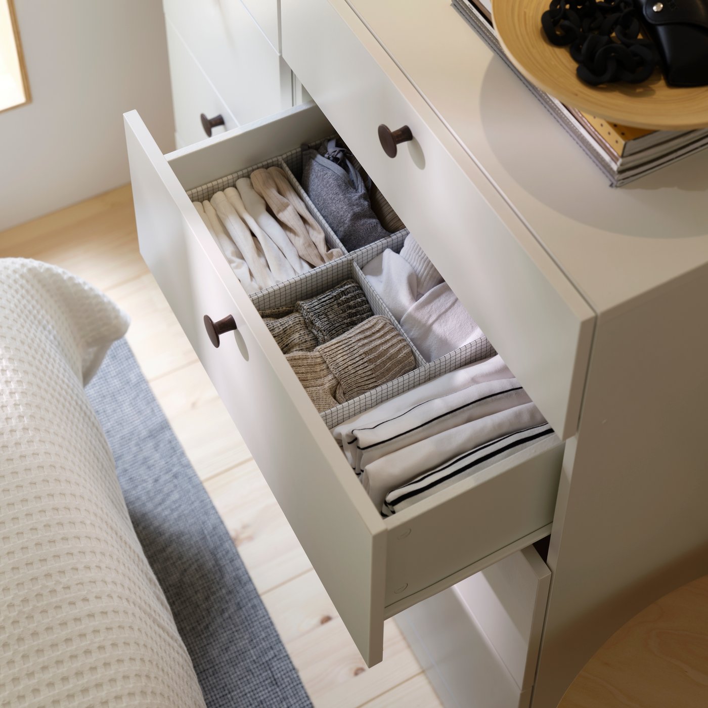An open drawer revealing a STUK box with compartments organising folded clothes inside a white chest of drawers.