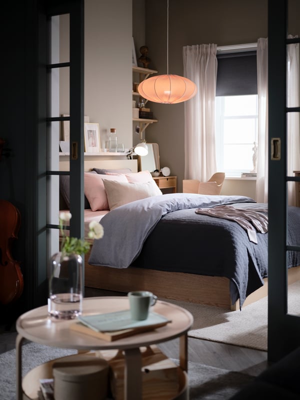 Parted glass doors open onto a bedroom with a MALM ottoman bed, dark-blue KOPPARBLAD bed linen, and a desk and chair.