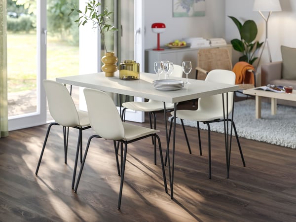 Une salle à manger lumineuse avec une table blanche entourée de chaises, de plantes et d'une lampe suspendue.