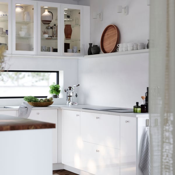 A bright kitchen with a wood floor has cabinets with glossy white RINGHULT fronts and wall cabinets with HEJSTA glass doors.