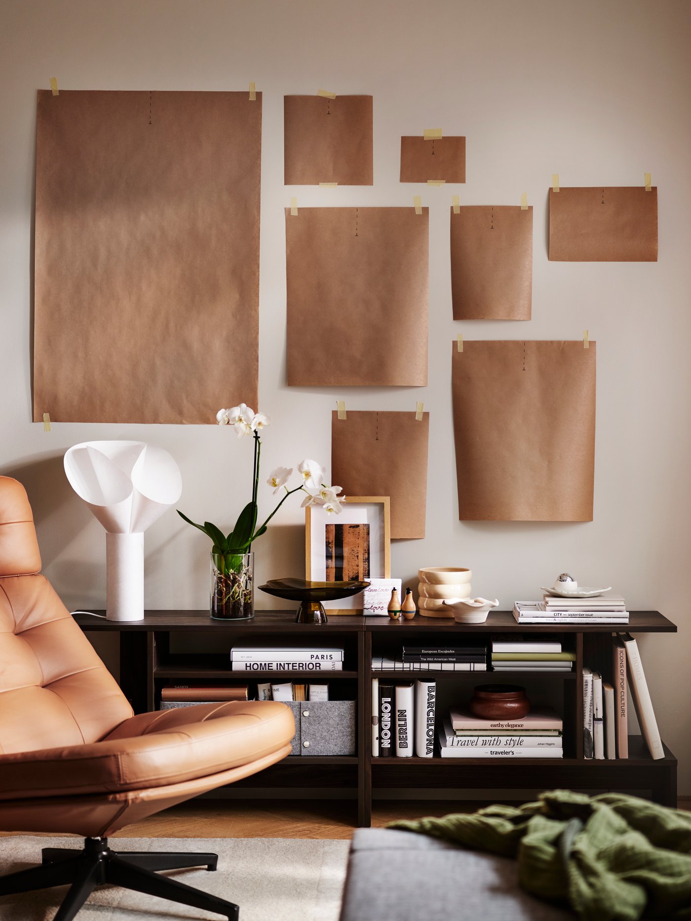 A cluster of taped-up paper templates on a wall above a golden-brown HAVBERG swivel armchair and HOLMERUD side tables.