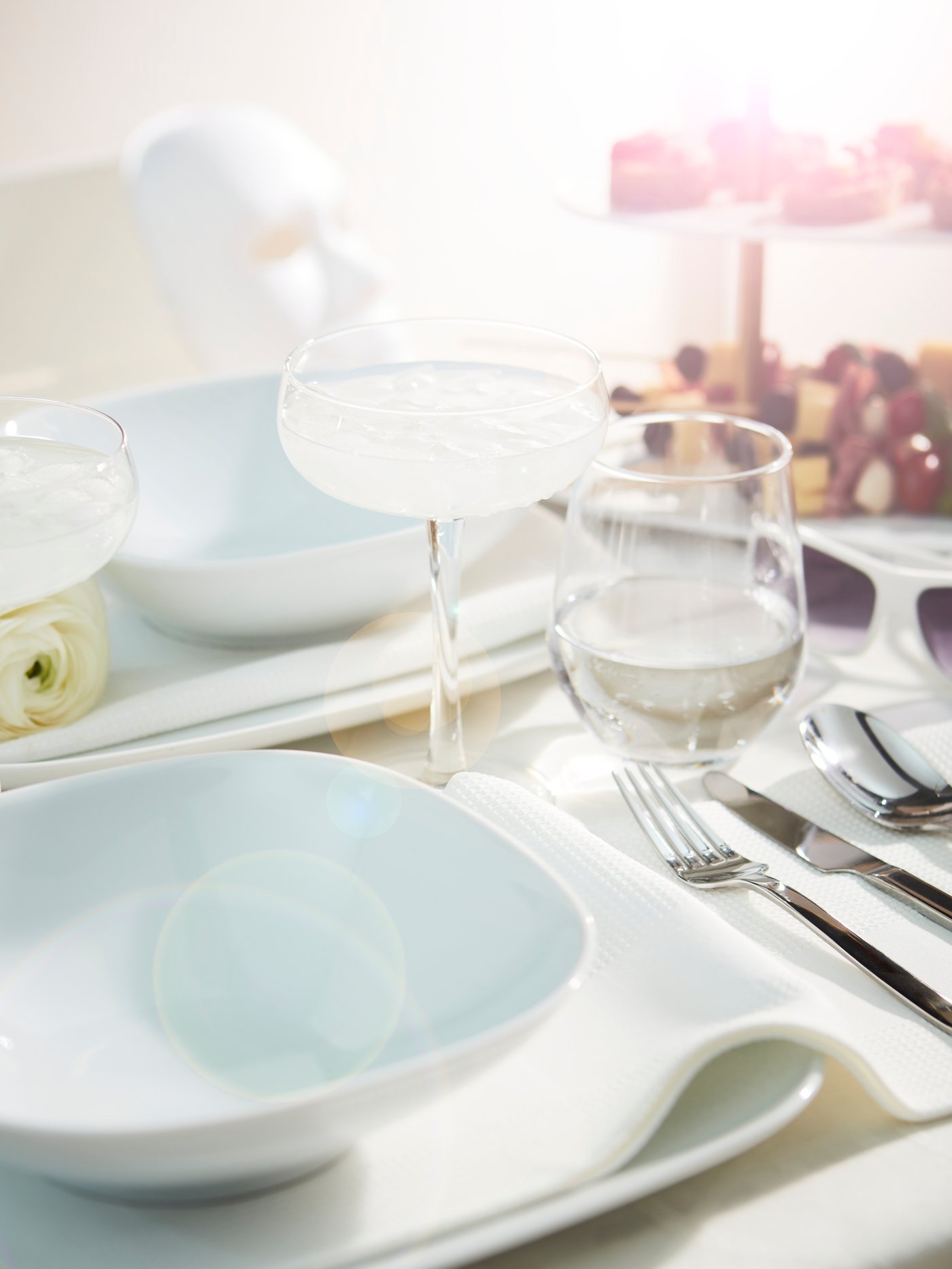 Plato hondo VÄRDERA en una mesa de comedor soleada para una cena donde todos aportan algo, con vasos y copas de champán.
