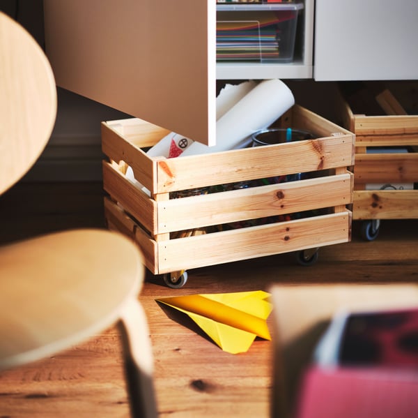 A pinewood KNAGGLIG box mounted on RILL castors is pulled out from under a white cabinet with one open door.