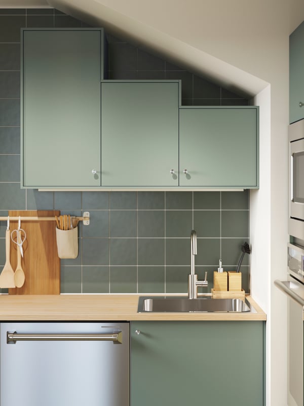 A kitchen with matte gray-green NICKEBO fronts has base cabinets and wall cabinets in various heights following a slanted ceiling.
