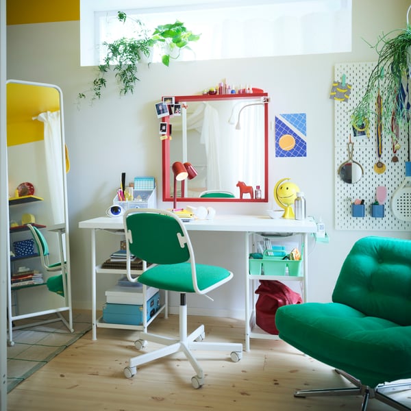 Colourful teen bedroom with a white desk, red mirror, green desk chair, green armchair, white pegboard and standing mirror.