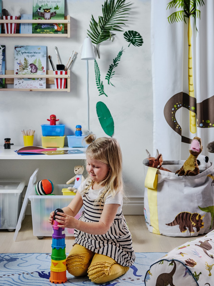 Habitación infantil con una persona de pie delante de un banco blanco de madera junto a una bolsa de almacenaje gris.