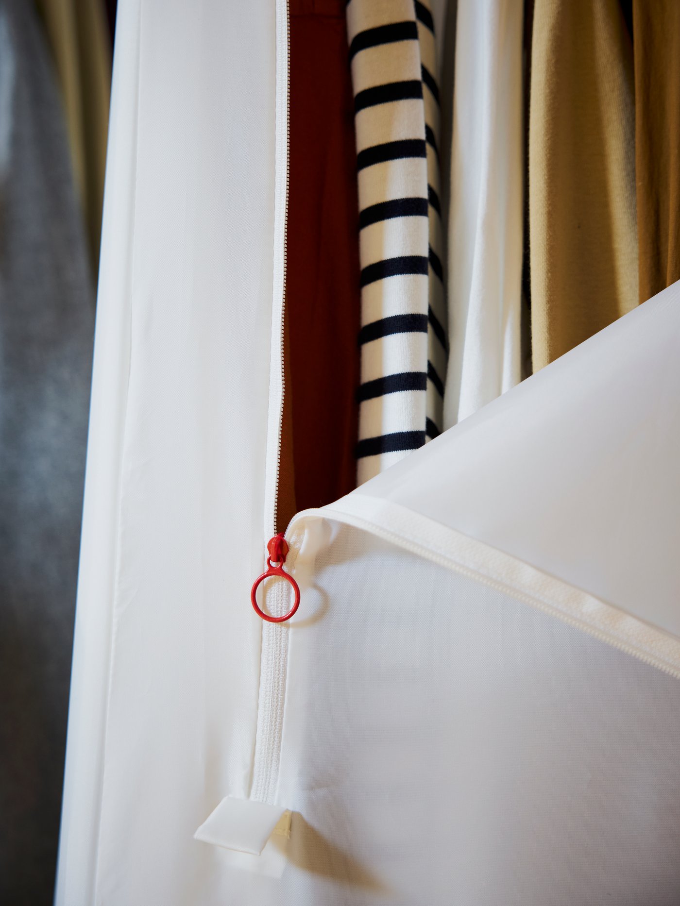 Gros plan sur une armoire-penderie VUKU en polyester blanc. La fermeture à glissière est à moitié ouverte, révélant quelques vêtements.