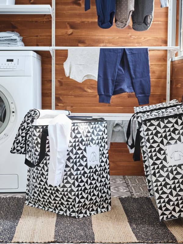 Two black and white designed laundry bags next to the washing machine with shirt labels on the front of them