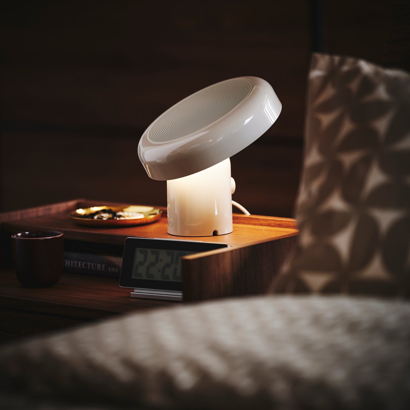 Närbild på ett nattduksbord med BLOMPRAKT bluetooth-högtalarlampa, som är den enda ljuskällan i det annars mörka rummet.