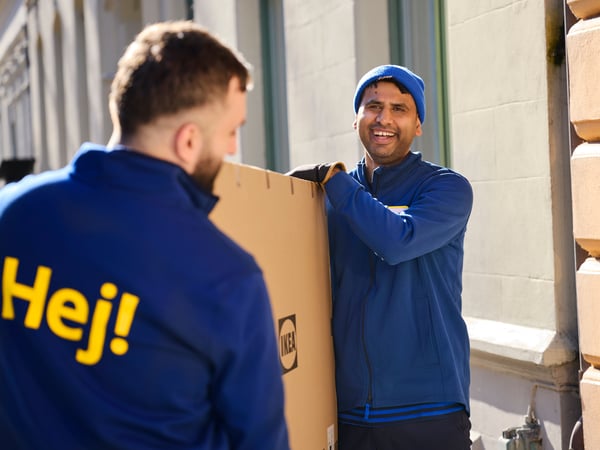 Deux collaborateurs IKEA portant un grand colis IKEA devant un domicile.