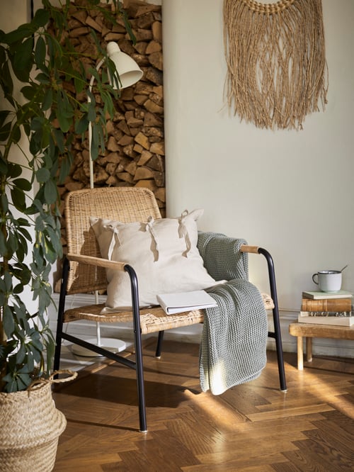 A modern living room featuring a rattan armchair, a cotton throw, a floor reading lamp, and a cushion cover.