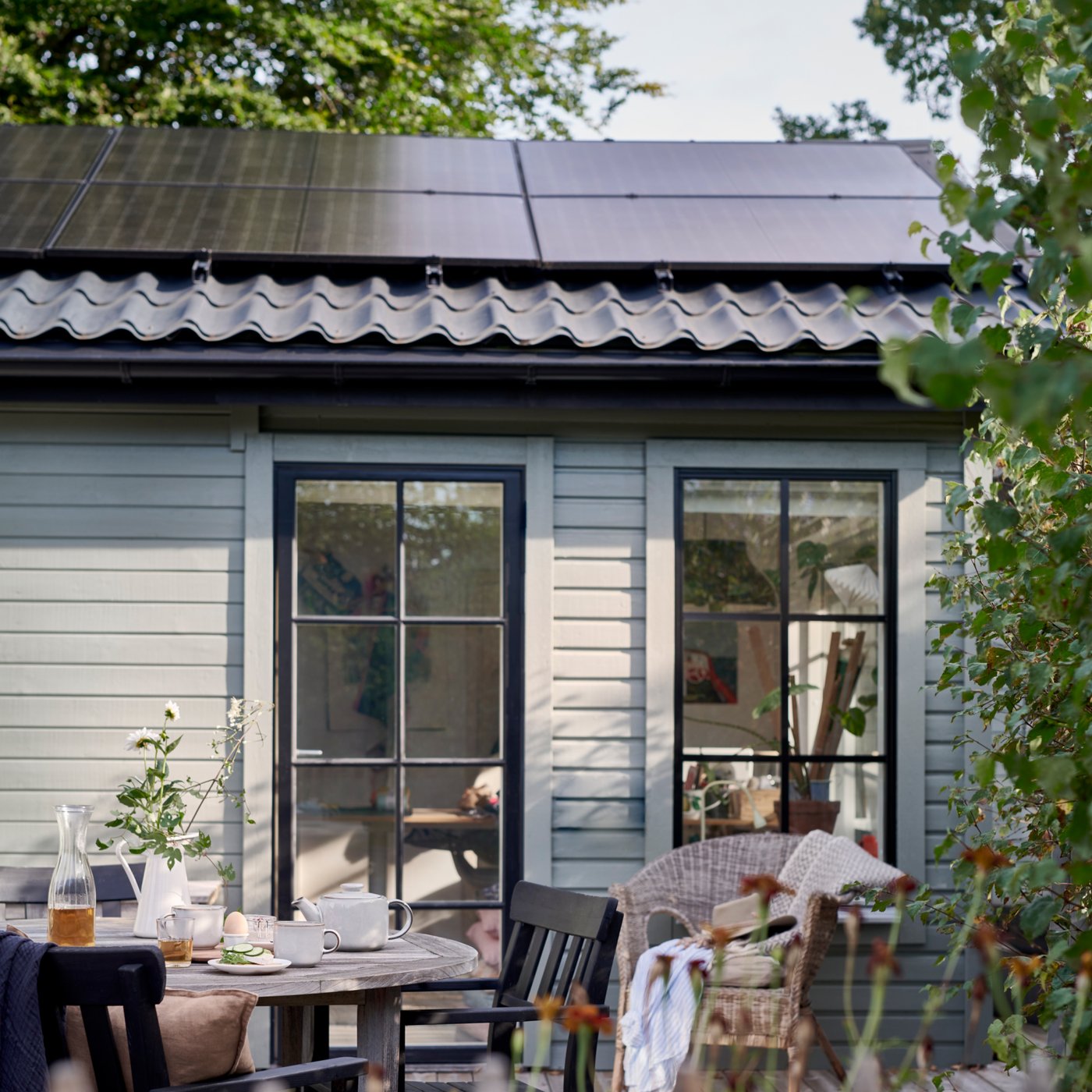 Cosy patio with a breakfast table in front of a house with two large windows and solar panels on the roof.