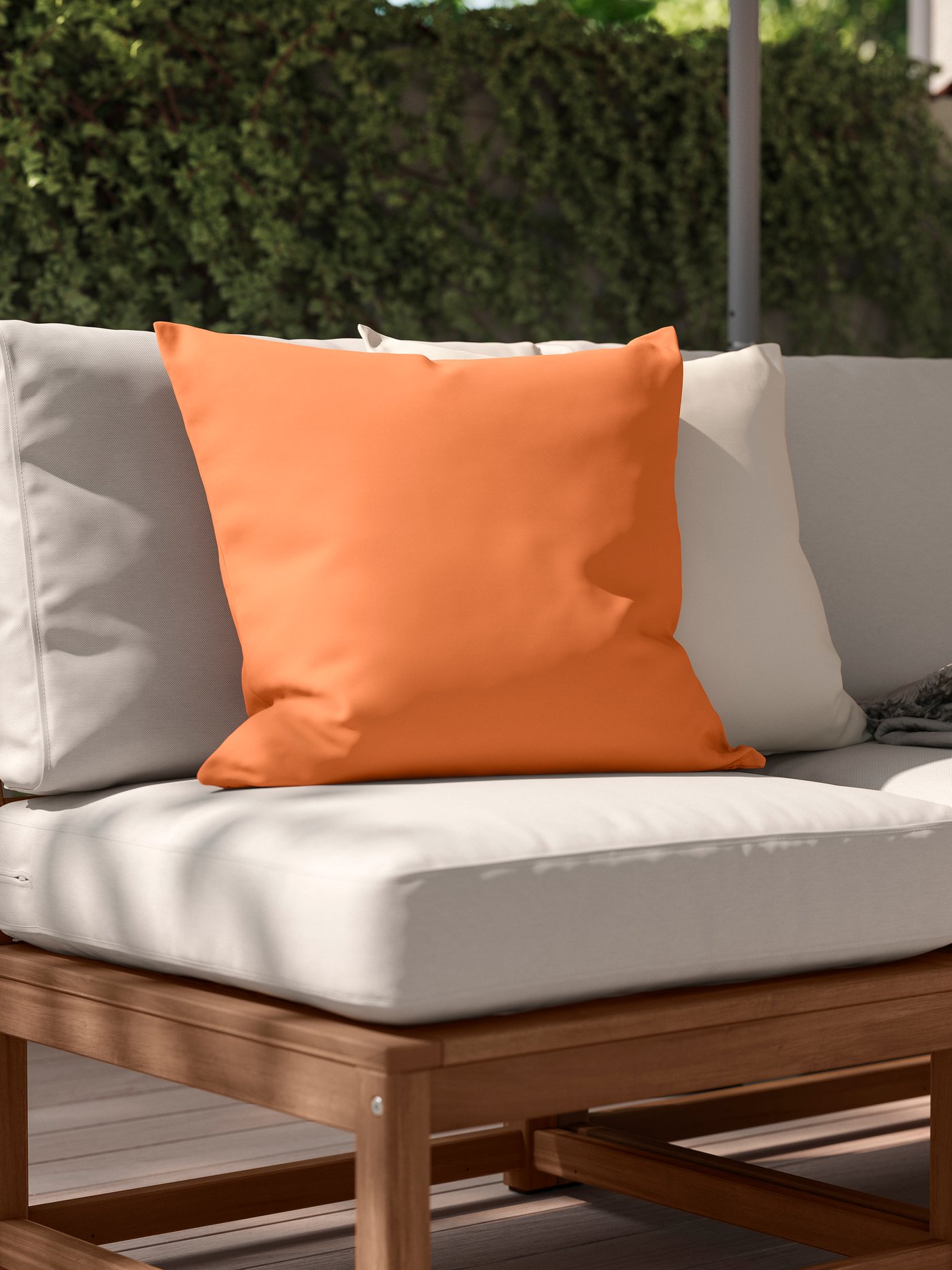 An orange HJÄRTERÖ cushion for indoor and outdoor use on a garden bench in the garden.