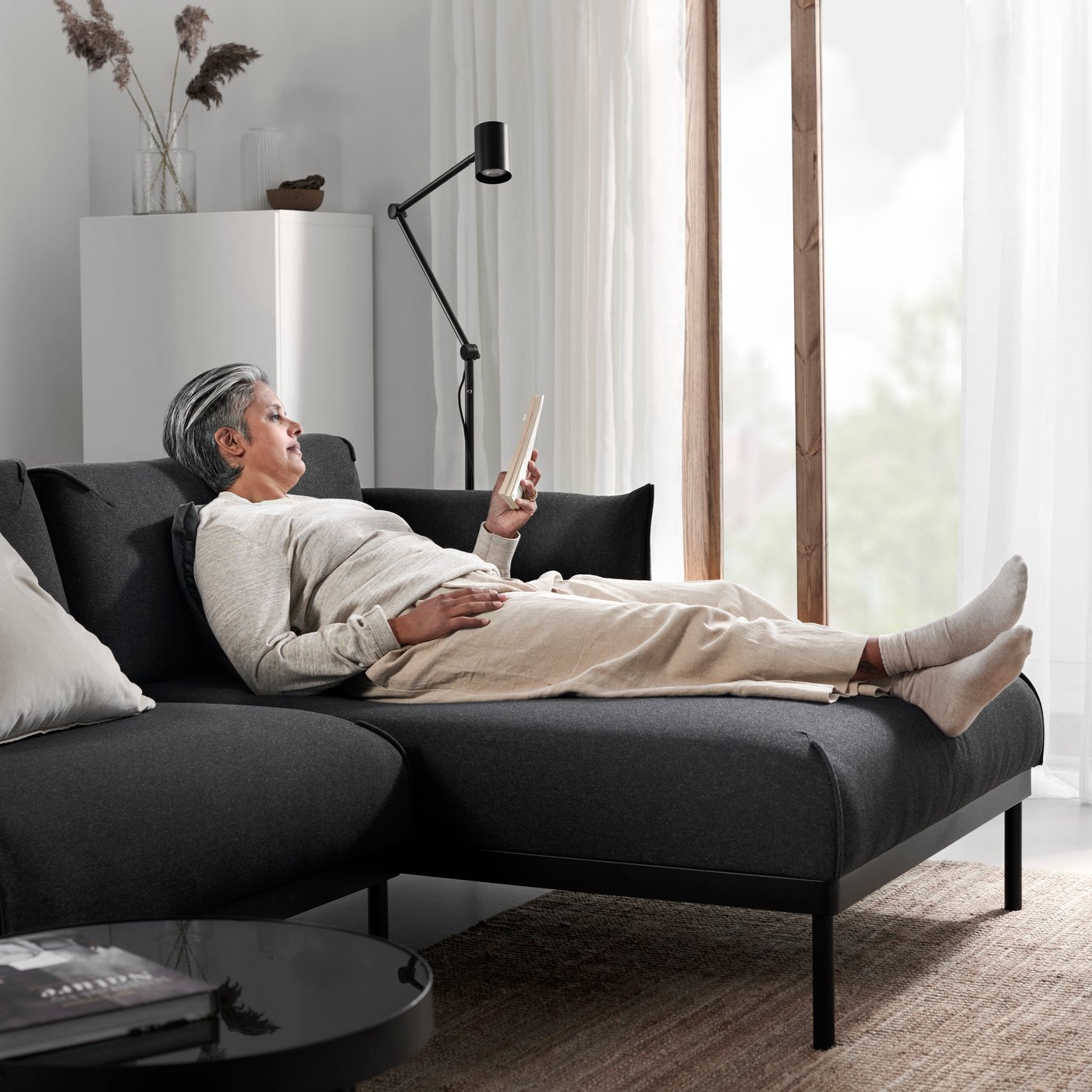 Szaro-czarna sofa czteroosobowa ÄPPLARYD z szezlongiem w przestronnym salonie z dużymi oknami.