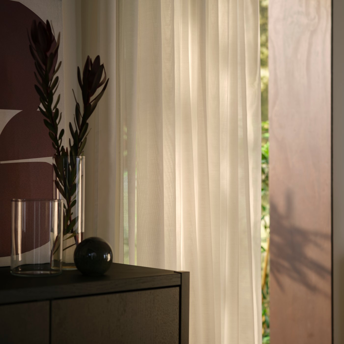 A living-room corner with a window covered by white STENFRÖ sheer curtains next to a dark-brown STOCKHOLM 2025 cabinet.