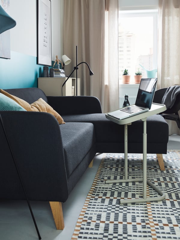 A LINANÄS sofa with chaise longue by a sunny window, with beige and turquoise cushions on it and a laptop stand in front.
