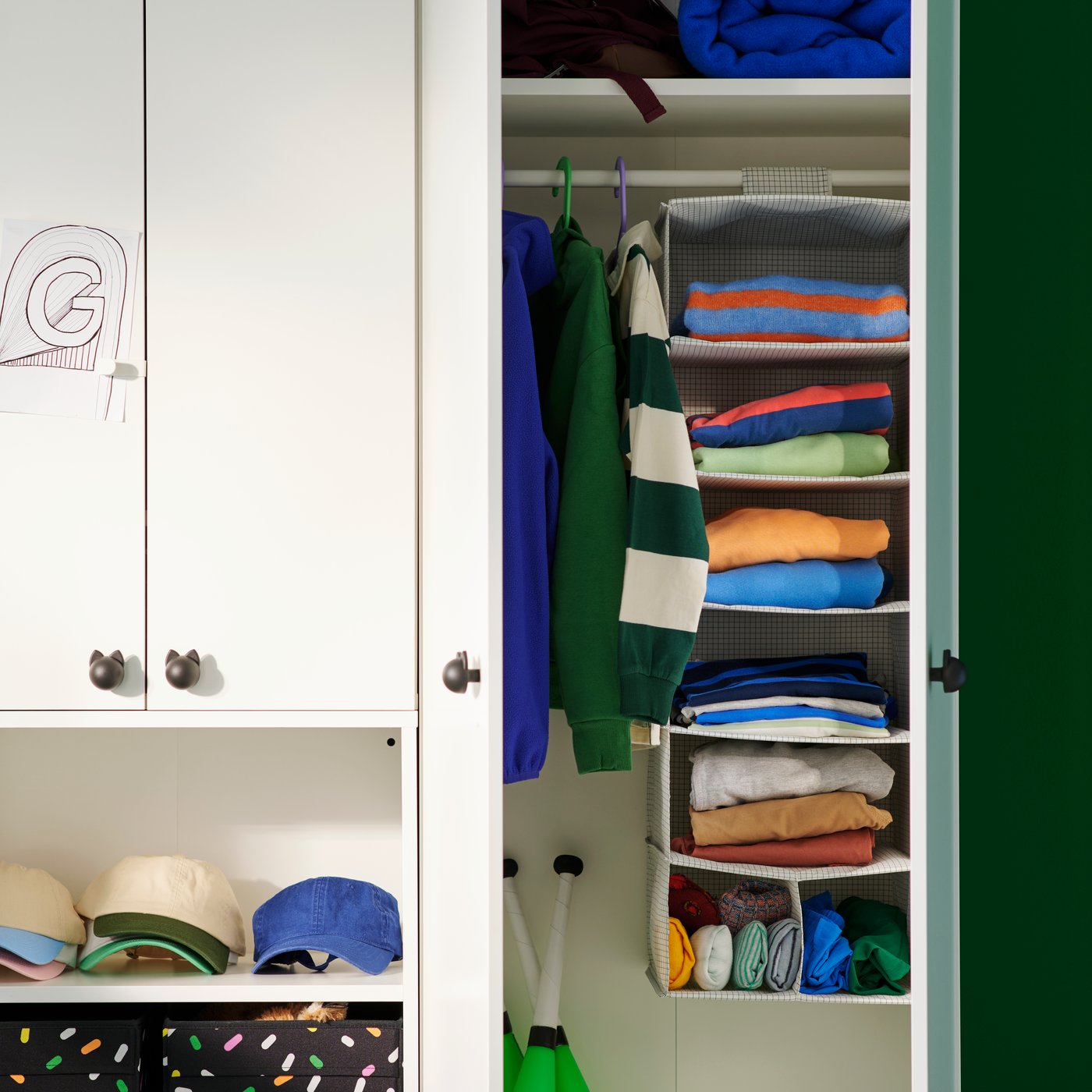 Inside a white wardrobe, a STUK hanging storage with seven compartments holds colourful folded clothes in a children's room.