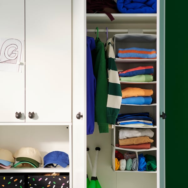 Inside a white wardrobe, a STUK hanging storage with 7 compartments holds colourful folded clothes in a children’s room.