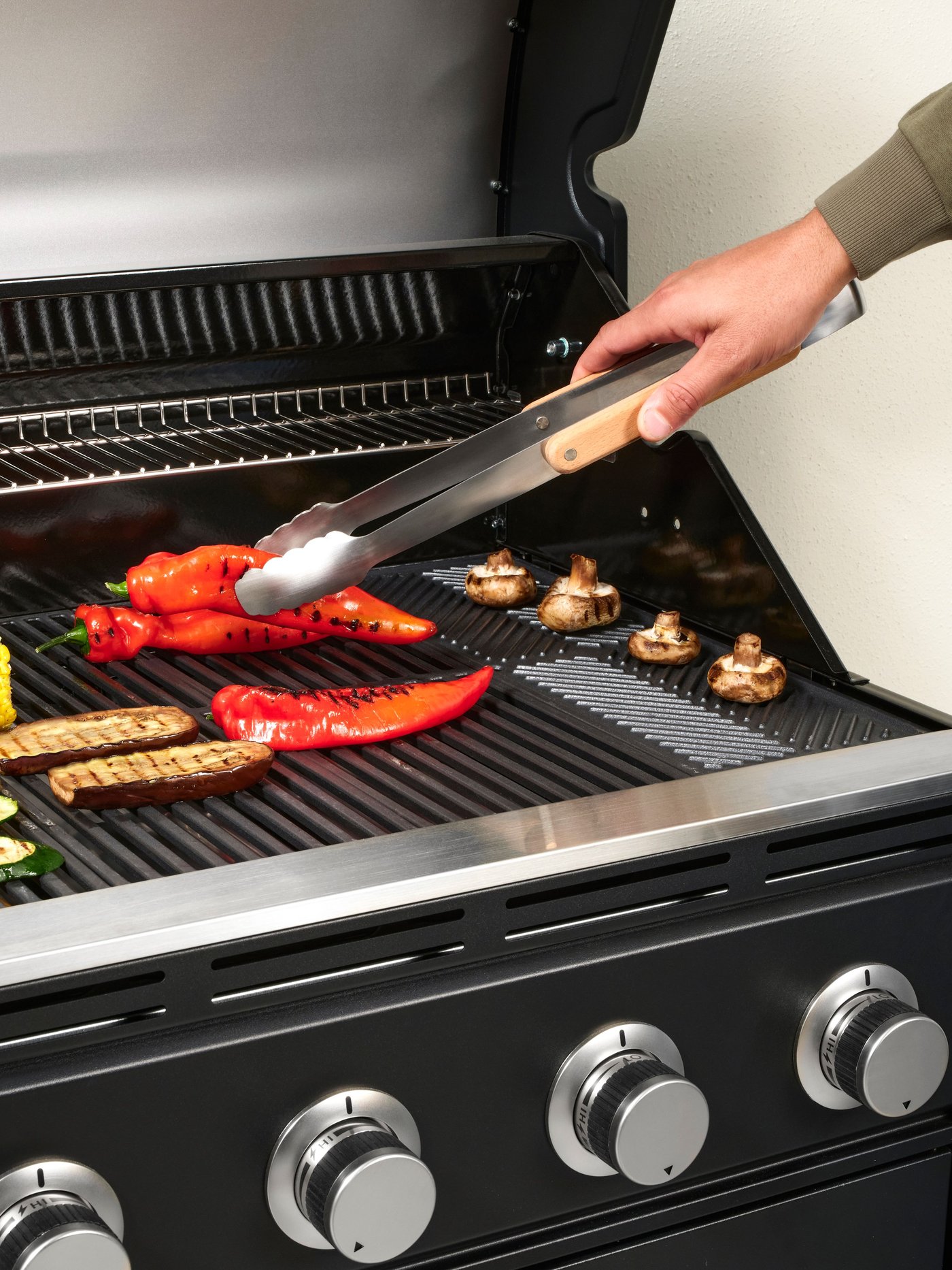 Una persona manipulando una tenaza GRILLTIDER para agarrar un ají sobre una parrilla IKEA.