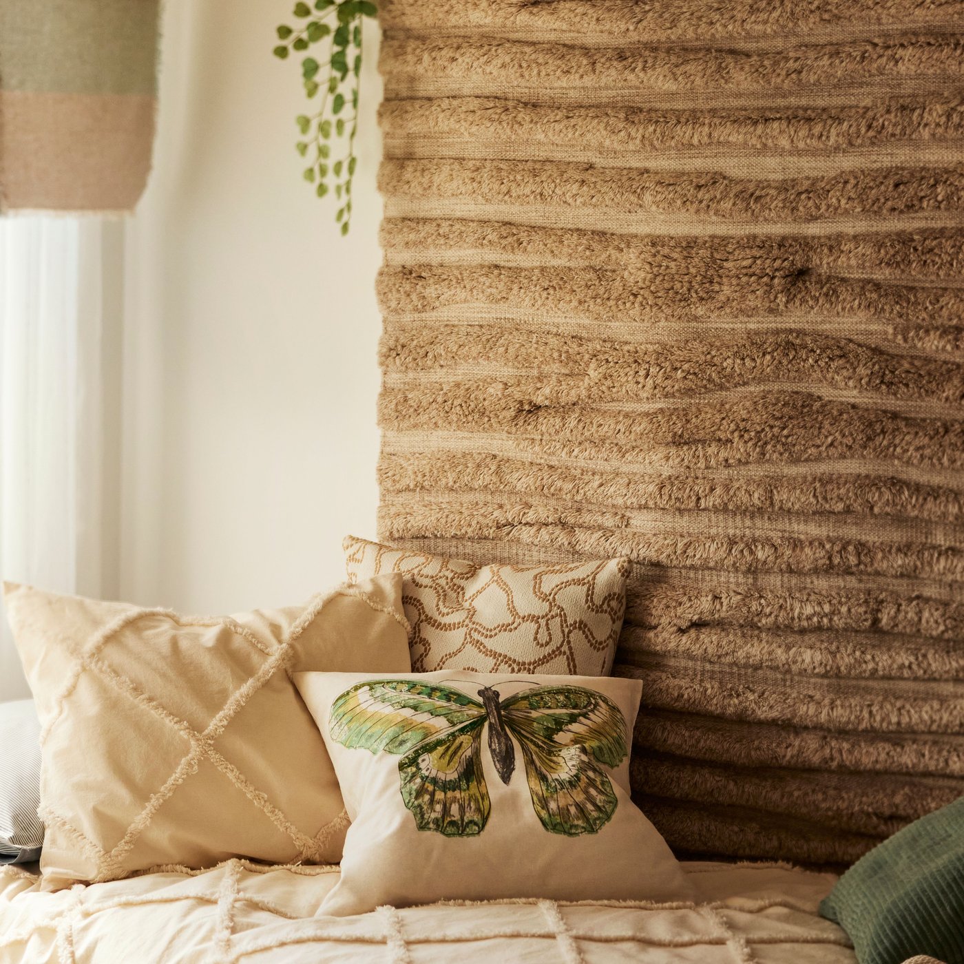 The wall of a bohemian-style bedroom has a beige, handwoven wool BANKKONTOR rug with a wavy pattern above a bed and cushions.