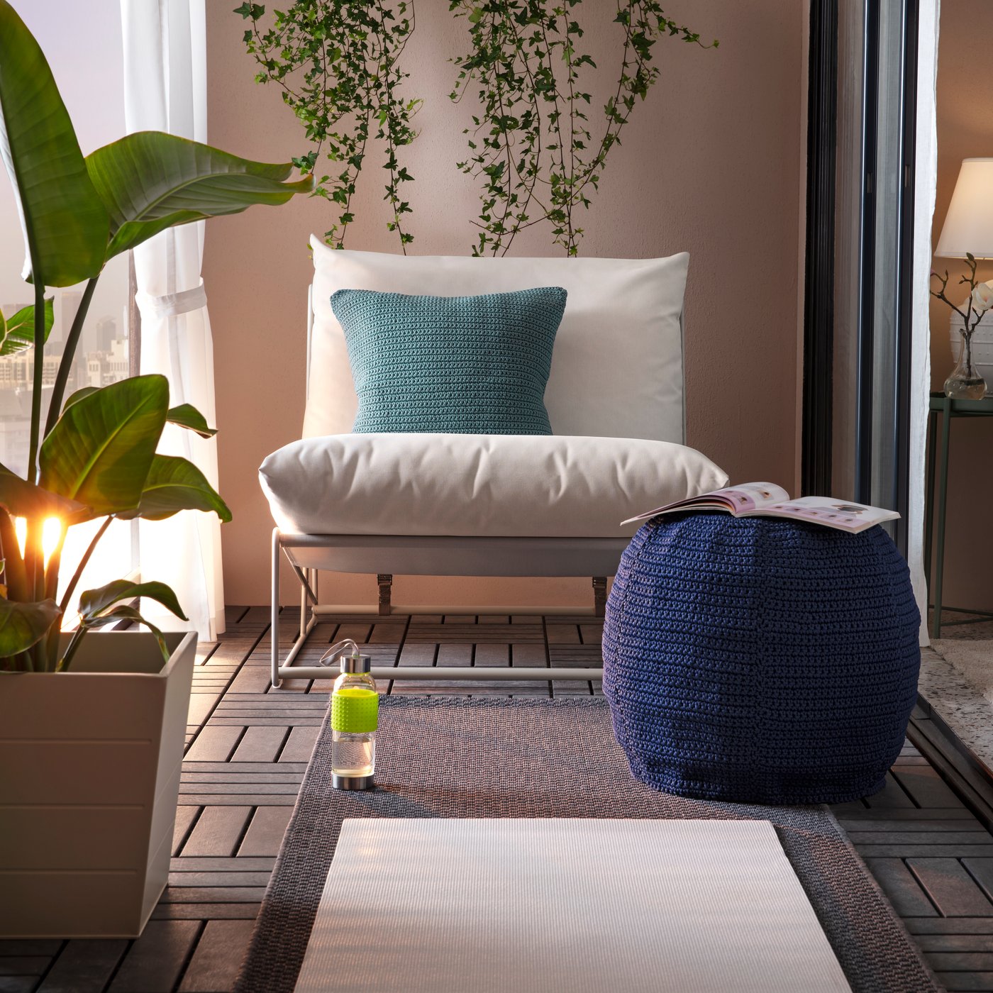 Poltrona HAVSTEN beige per interno o esterno con cuscino verde acqua, su un balcone arredato con tappeti, pouf blu e piante verdi.