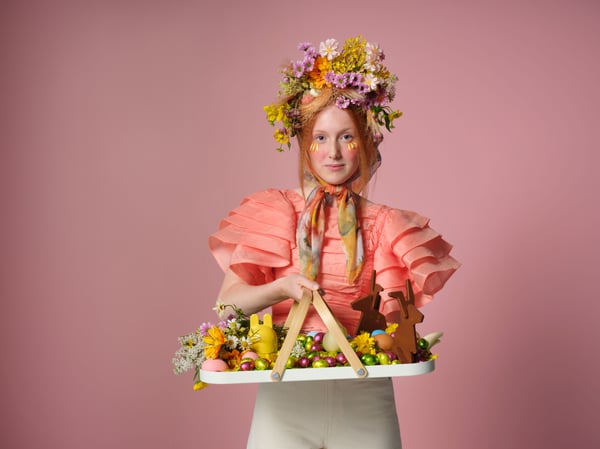 Femme vêtue d’une tenue de Pâques, tenant un plateau avec des fruits et des chocolats.