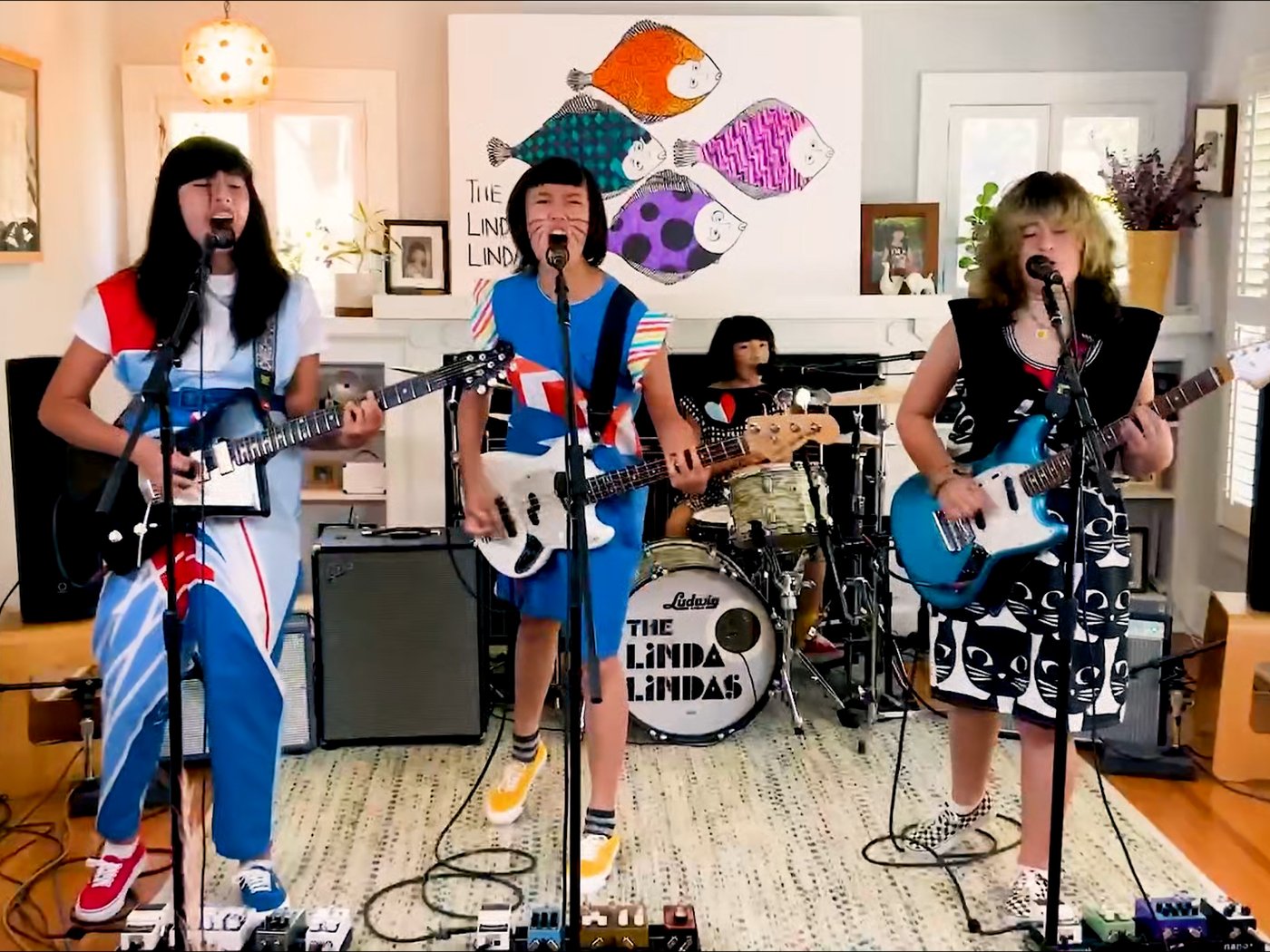 Članice benda The Linda Lindas u šarenoj odeći pred mikrofonom. 