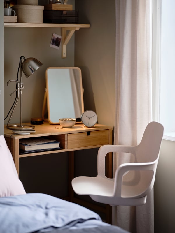 Bedroom with a white-beige ODGER swivel chair standing by a NORDKISA dressing table with a lamp and mirror on it.