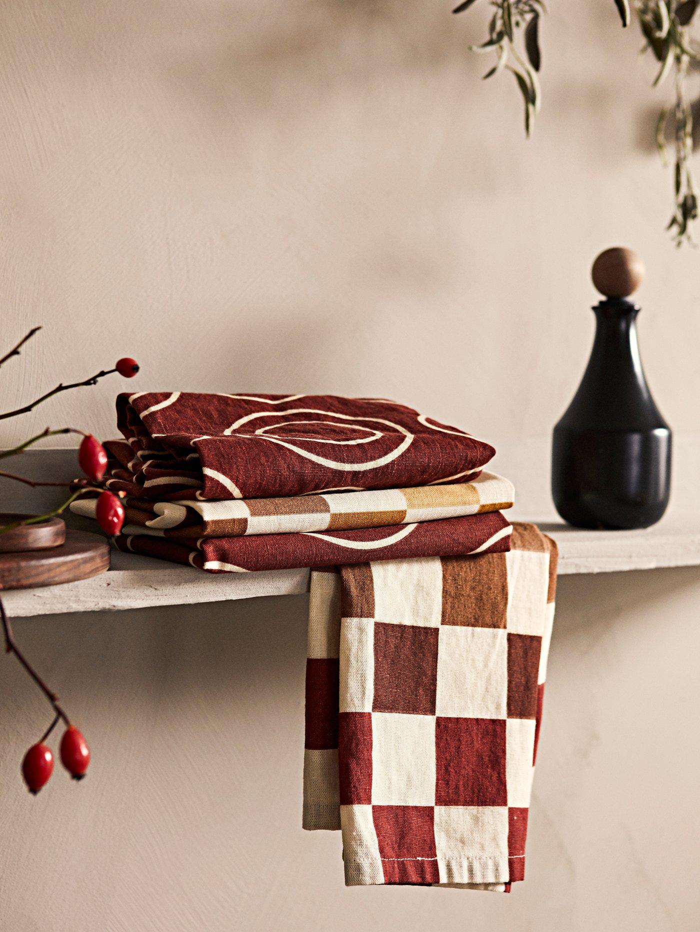 Tuala pengesat KRÖSAMOS yang berlipat dengan botol KRÖSAMOS berwarna hitam terletak di atas para kayu di dapur.