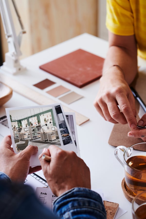 Gros plan sur une main tenant des Polaroïds de bureaux, l’autre main tient un crayon de papier