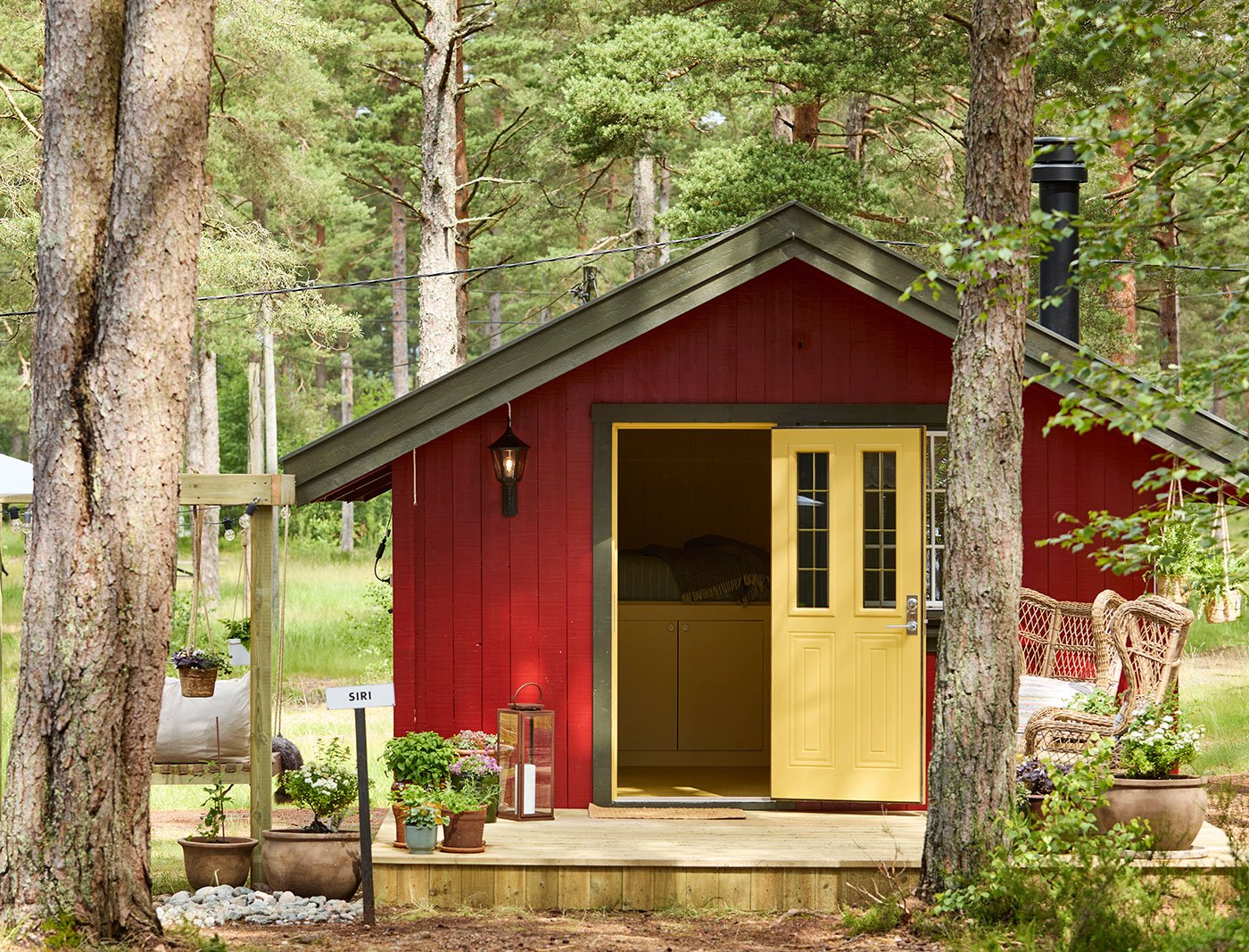 Petit chalet rouge avec une porte jaune, nichée au milieu des arbres dans une forêt.
