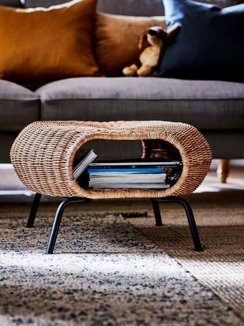 Living room close-up of a beige footstool with storage made of rattan, placed on a rectangular rug flatwoven.