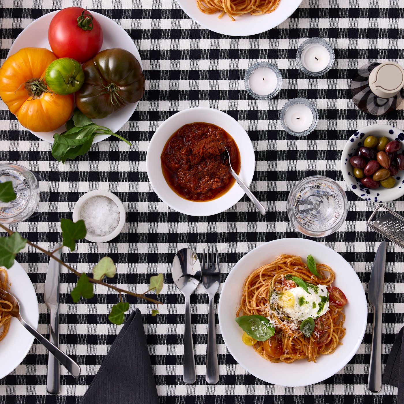 Vita tallrikar och skålar från OFTAST-serien är fyllda med mat och placerade på en svartvit rutig duk.