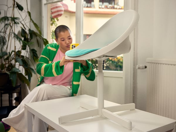 A person in a green and white striped sweater is taking a photo of a white modern chair with a blue cushion.